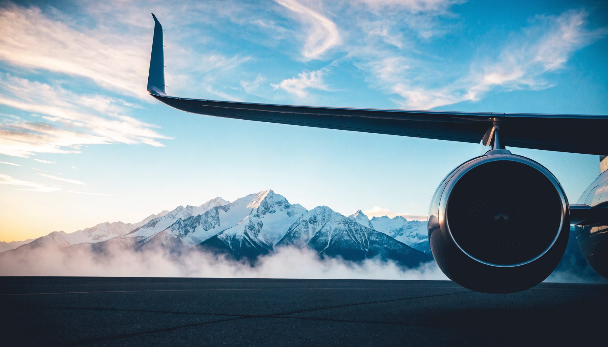 Private jet engine and wing on an apron at dawn, snow-covered peaks behind