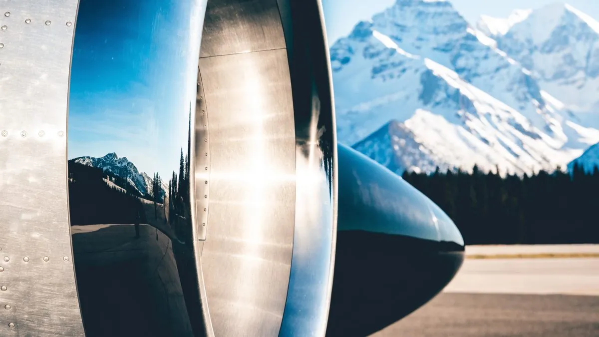Polished jet engine cowling reflecting snowy mountains and pine forest